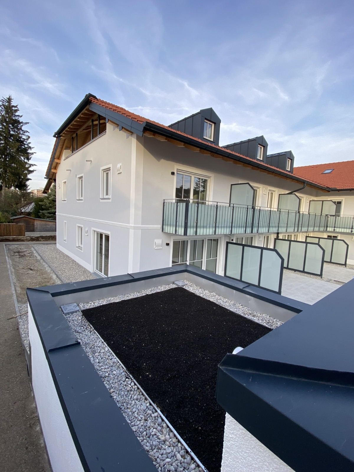 Neubau mit verblechten Gauben und Balkonen, im Vordergrund ein begrüntes Flachdach mit Attikaverblechung