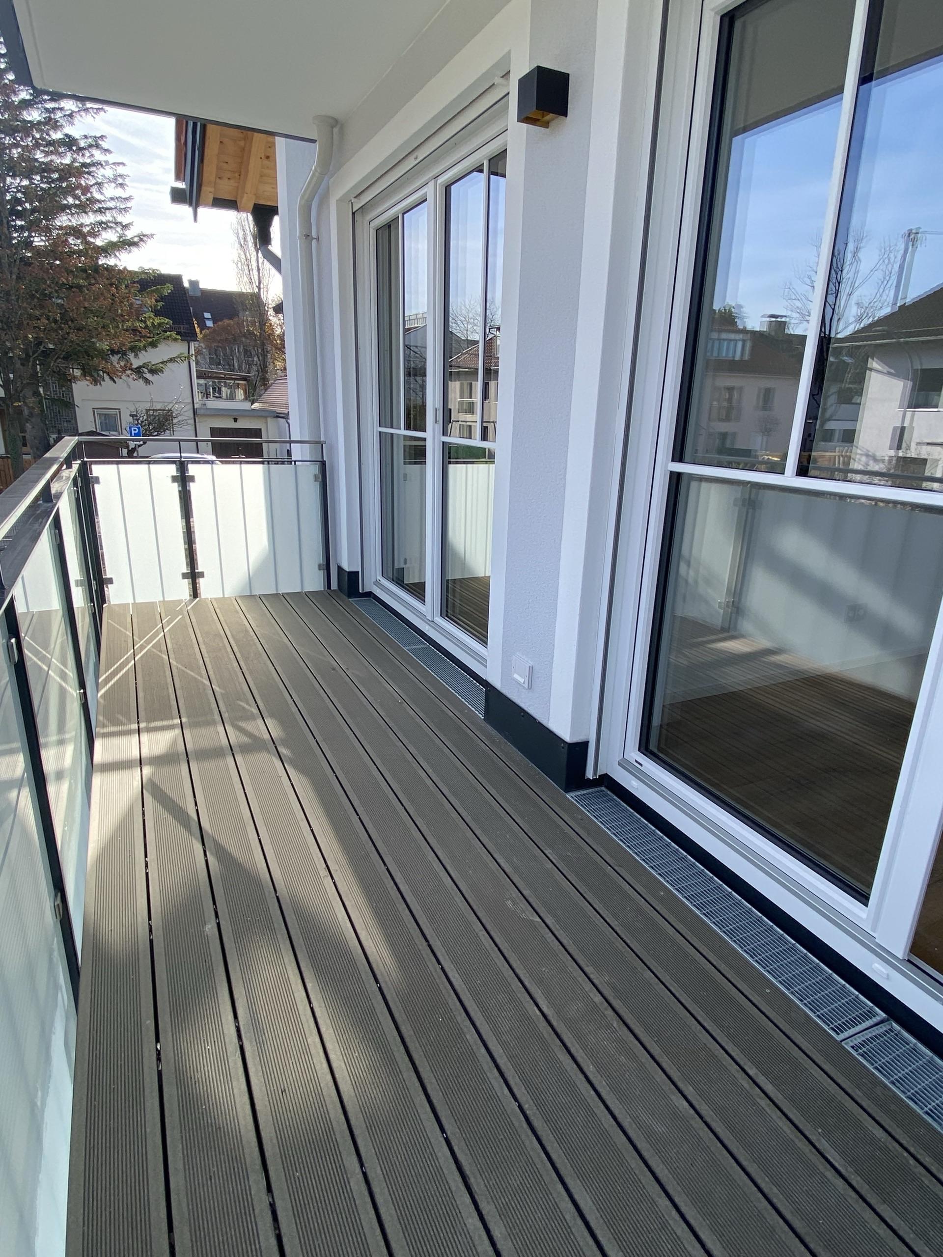 Neuer Balkon mit grauem WPC-Belag, Glasgeländer und bodentiefen Fenstern
